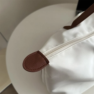 White nylon tote bag with brown leather handles on a minimalist white table