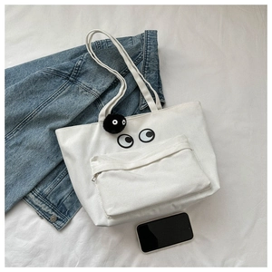 Detail of white canvas tote with cartoon eyes print and black plush pompom charm