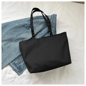 Flat lay of a spacious black canvas tote bag styled with a denim jacket on white background