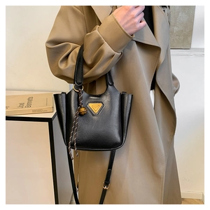 Detail of black leather bucket bag with triangle metal buckle and woven bell charm