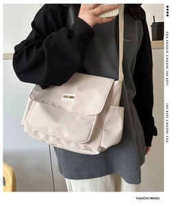 Dettaglio della borsa a tracolla in tela beige con patta e ricamo decorativo