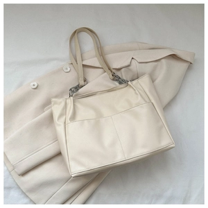 Close-up of cream tote bag featuring silver chain straps and soft faux leather texture