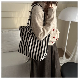 Detailed view of large black and white striped canvas tote bag worn by a model