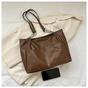 Detail of a brown faux leather tote bag with large outer pockets and silver chain straps