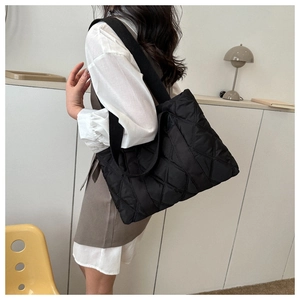Model wearing a large black quilted tote bag with rhombus pattern and wide shoulder straps