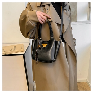 Detail of black textured bucket bag with golden triangular hardware and woven knot charm