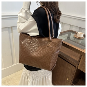 Close-up of a large dark brown woven tote bag featuring deep texture on soft leather straps