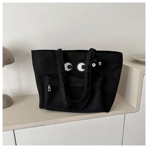 Detail of black canvas tote bag featuring cartoon eyes patch and plush ball charm decoration