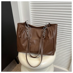 Detail of a brown leather tote bag showing silver metal chain straps and side pocket design