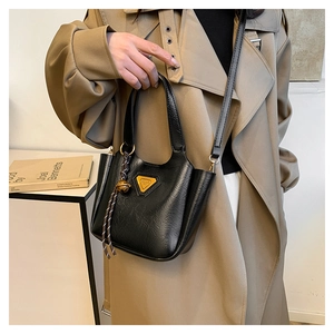 Detail of black crossbody bucket bag with gold triangle logo and woven pendant charm