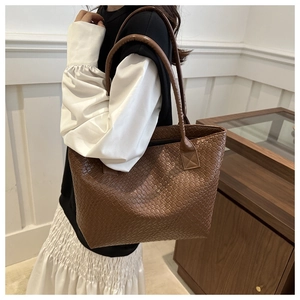 Brown woven texture tote bag detail showing large capacity and leather handles on model