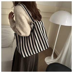 Classic black and white striped canvas tote bag shown on a model in a cozy indoor setting