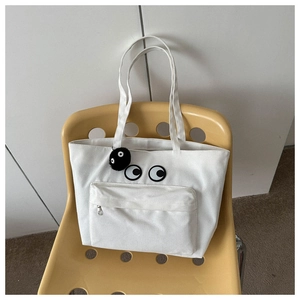 Close-up of white canvas tote with cartoon eyes and a plush dust sprite keychain charm