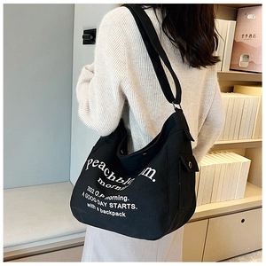 Detail of black canvas tote bag showing side snap pocket and white typography print