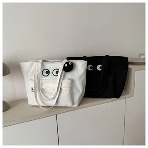 Detail of canvas tote bags in black and white with eye print and plush pendant