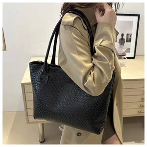 Detail of black woven texture on a large capacity tote bag worn with a casual trench coat