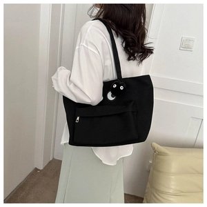 Detail of black canvas tote bag with front zipper pocket and cute plush coal ball charm