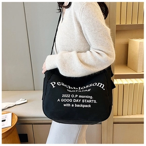 Detail of large black canvas bag with white letters and adjustable strap in lifestyle setting