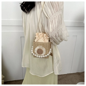 Detail of straw bucket bag featuring sunflower embroidery and a faux pearl handle