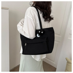 Detail of large black canvas tote bag with fuzzy sprite charm and front zipper pocket