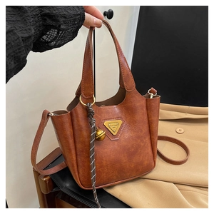 Detail of brown vintage wax leather bucket bag with metal plate and bell charm