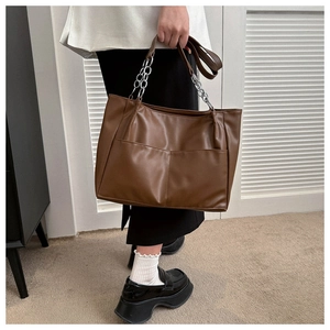 Close-up of brown soft leather tote bag featuring front pockets and silver chain handle