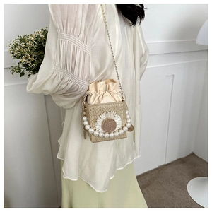 Detail of straw woven crossbody bag with sunflower decor and pearl handle on model