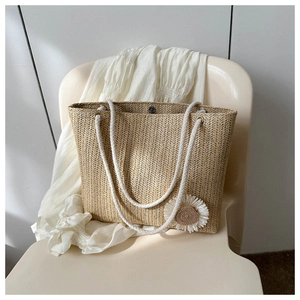 Detail of beige straw tote bag featuring a white daisy flower and metal magnetic closure