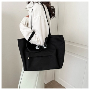 Close-up of black canvas tote bag with large eye embroidery and front zipper pocket