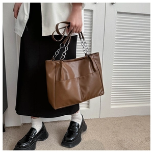 Detail of dark brown tote bag with metal chain and front pockets worn by model