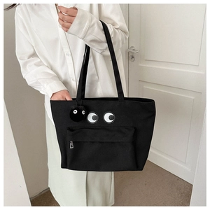 Detail of black canvas tote bag featuring large eye embroidery and a fuzzy soot sprite charm