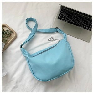 Top view of a light blue crescent crossbody bag with a cute white charm on fabric