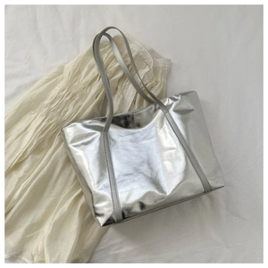 Close-up of a silver metallic tote bag with sleek shoulder straps on white fabric