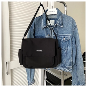 Detail of a black canvas messenger bag with brand logo tag and adjustable shoulder strap