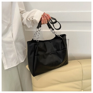 Detail of black leather tote bag featuring front twin pockets and silver metal chain strap