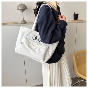 Close-up of white canvas tote bag featuring embroidered eyes and functional front zipper