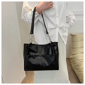 Detail of black tote bag featuring dual front pockets and silver chain leather strap