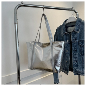 Detail view of silver metallic tote bag with smooth texture hanging on steel hanger