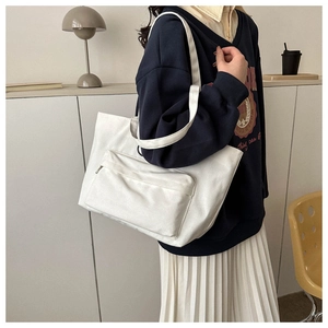 Detail of white canvas tote bag featuring a functional front zipper pocket and shoulder strap