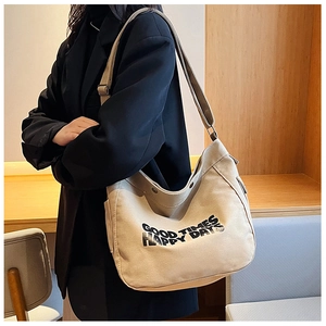 Model wearing a large beige canvas tote bag with Good Times print over a black suit jacket