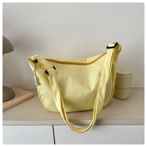 Detail view of light yellow canvas crescent bag with adjustable strap and silver chain tag
