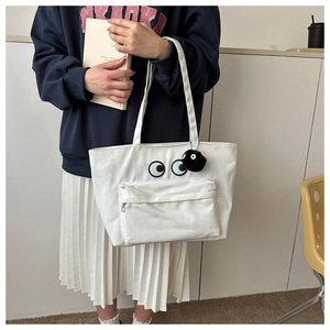 Detail of white canvas tote bag with eye embroidery and plush coal sprite charm
