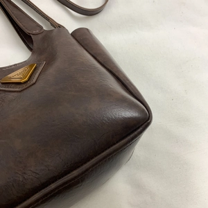 Vintage brown leather bucket bag with a golden triangular metal plaque on a white background
