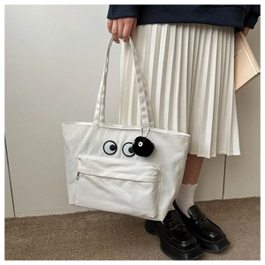 Detail of white canvas tote bag featuring large eye print and black pompom charm accessory