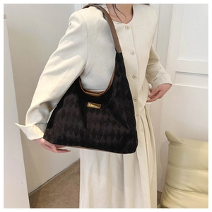 Detail of black quilted shoulder bag with brown leather strap and metal plate