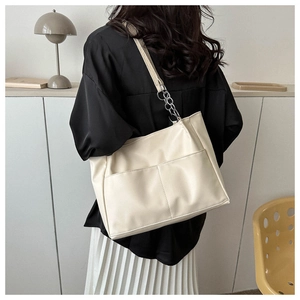 Detail of off-white tote bag featuring metallic chain strap and front utility pockets