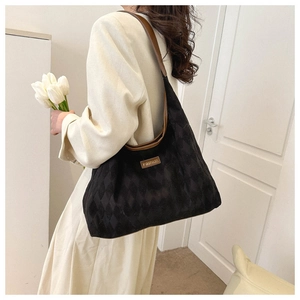 Close-up of black quilted tote bag with brown leather straps and fashion metal plaque