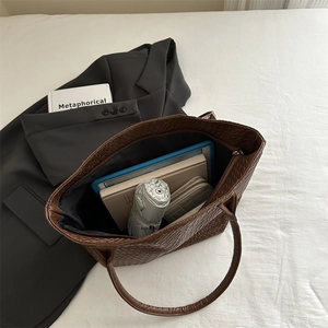 Brown woven leather tote bag with large capacity for daily essentials shown on white bedding