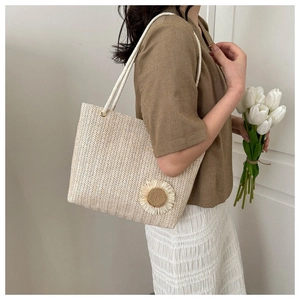 Detail of woven straw tote bag with sunflower decoration and rope handle held by model