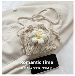 Mini straw bucket bag with crochet flower detail and tassels next to smartphone for scale